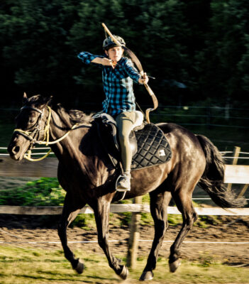 Reiterin auf galoppierendem Pferd, mit Pfeil und Bogen auf ein Ziel schießend.